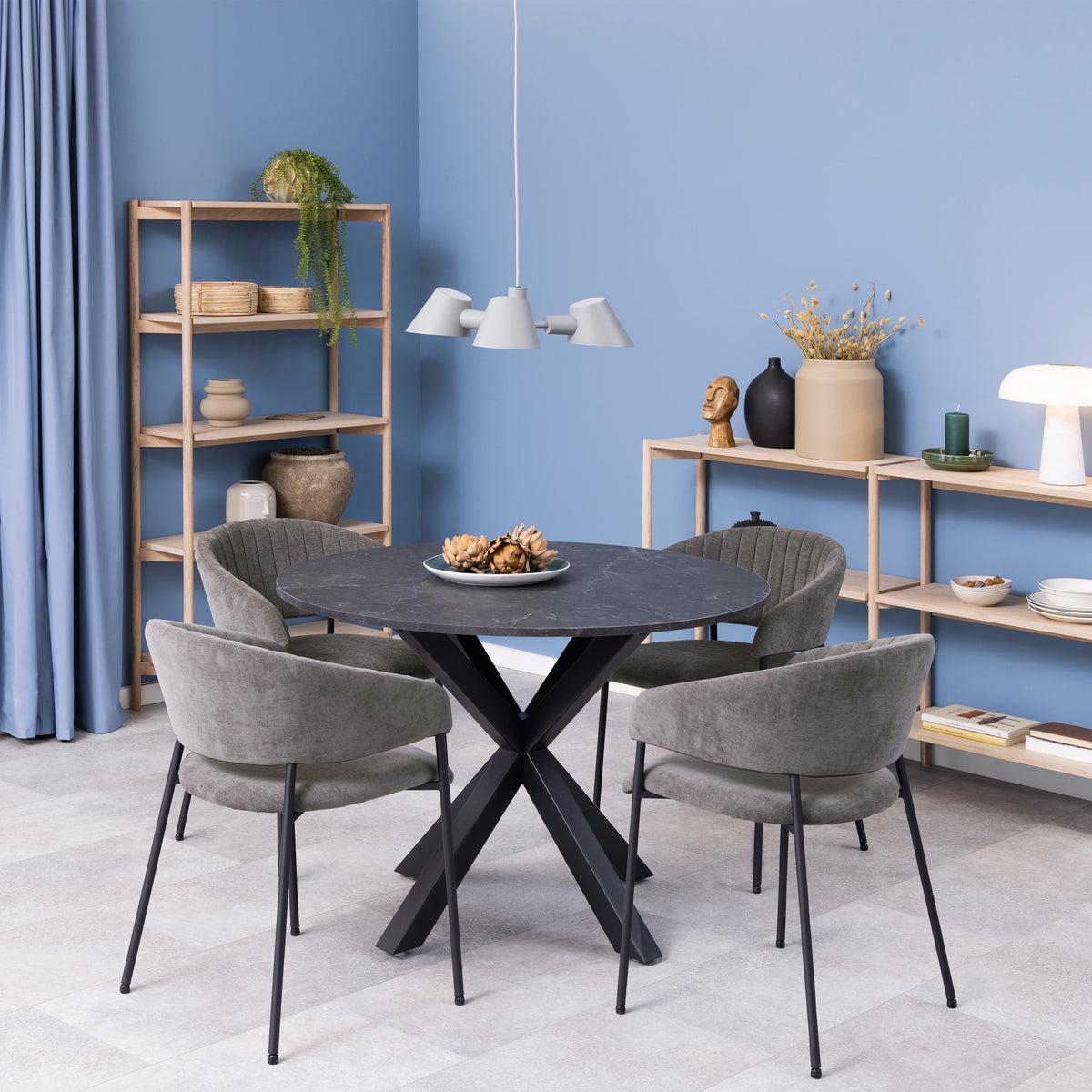 Set di sedie Brooke grigie attorno a un tavolo rotondo nero in un ambiente contemporaneo con scaffali in legno chiaro.