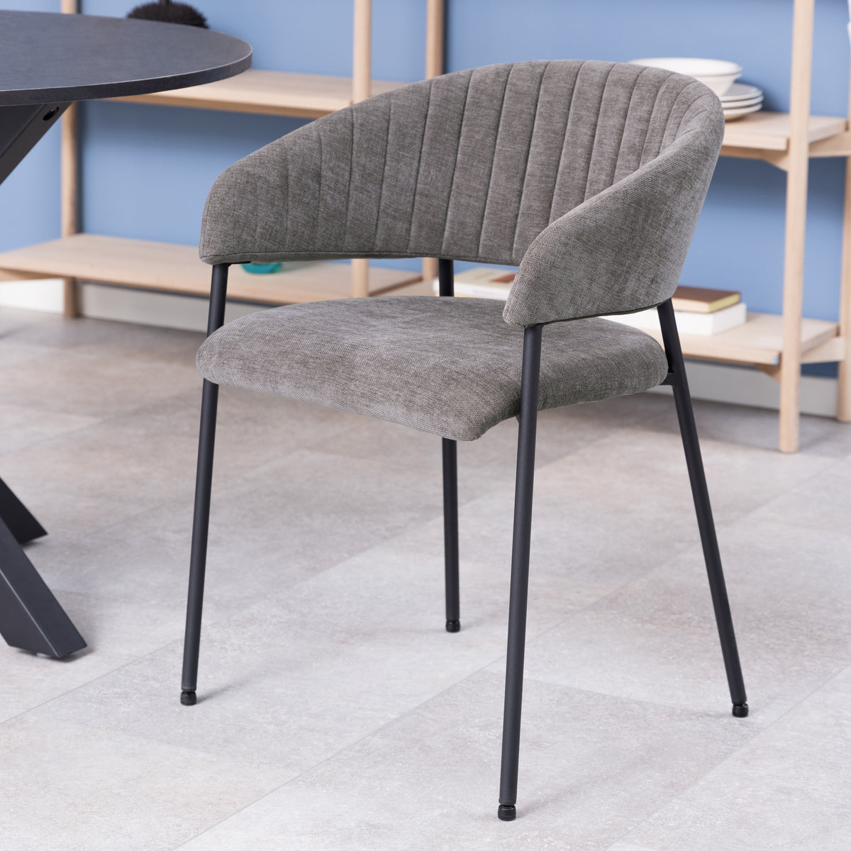 Sedia Brooke grigia in un ambiente moderno con pavimento chiaro e tavolo nero, perfetta per spazi contemporanei.