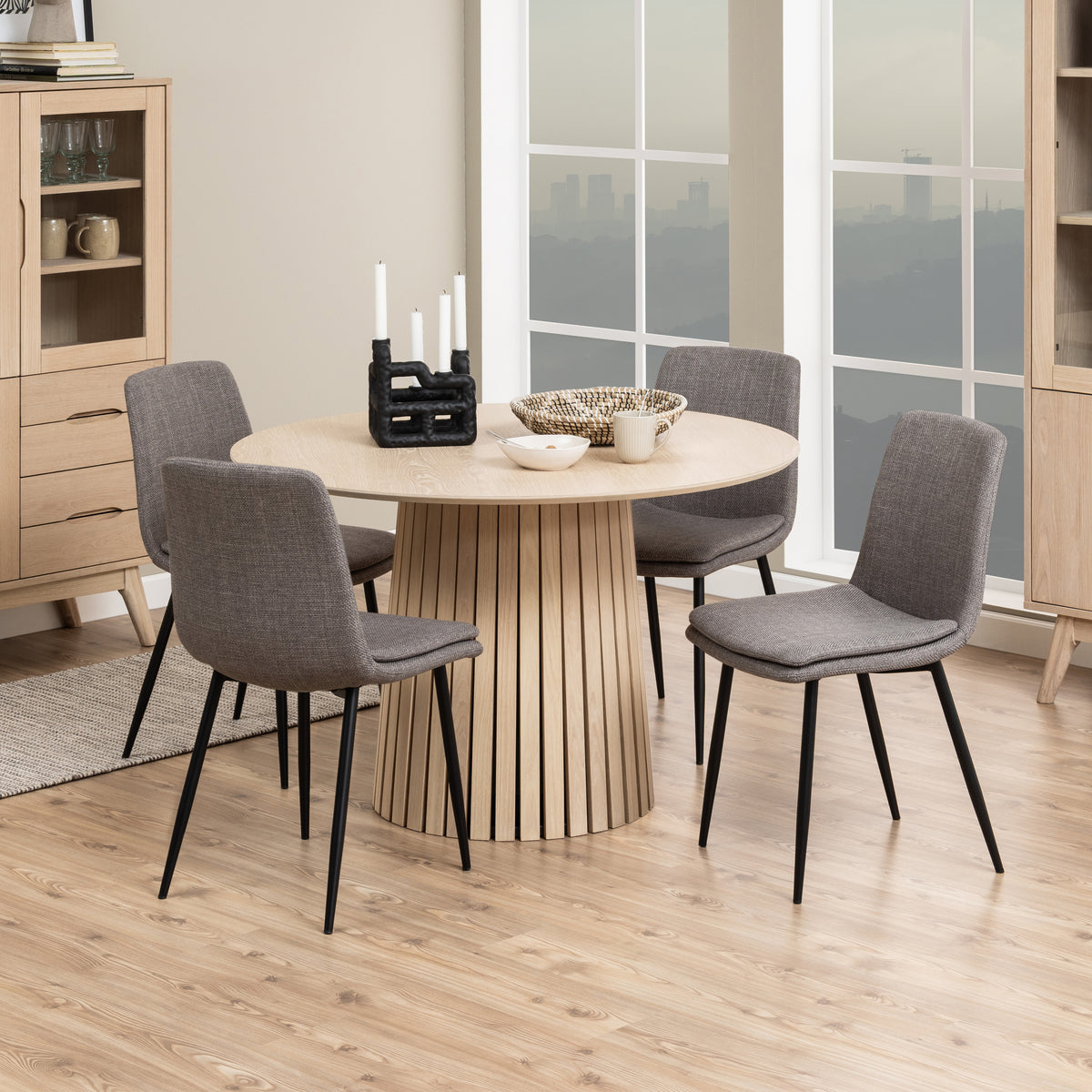 Set di quattro Sedie Bella grigie attorno a un tavolo rotondo in legno chiaro, ideale per sale da pranzo contemporanee.