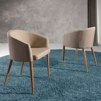 Due sedie Lowell in tessuto beige con gambe in legno su tappeto blu, perfette per ambienti moderni.