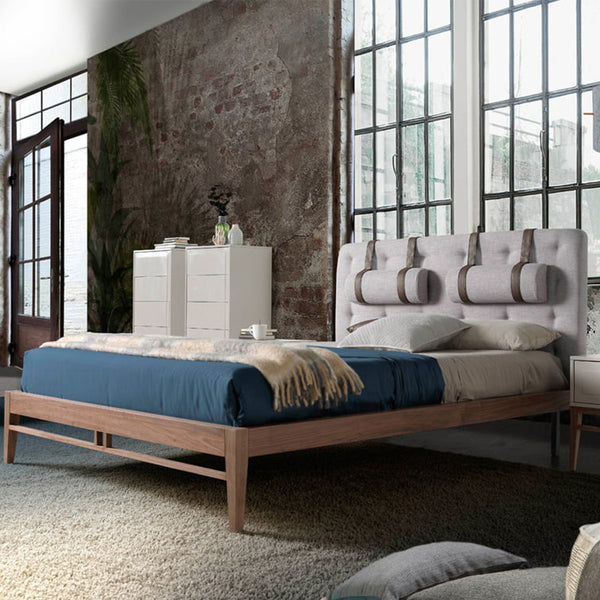 Letto Lusiana in una camera moderna con pareti in mattoni, struttura in legno noce e testiera grigia capitonné con dettagli in similpelle.
