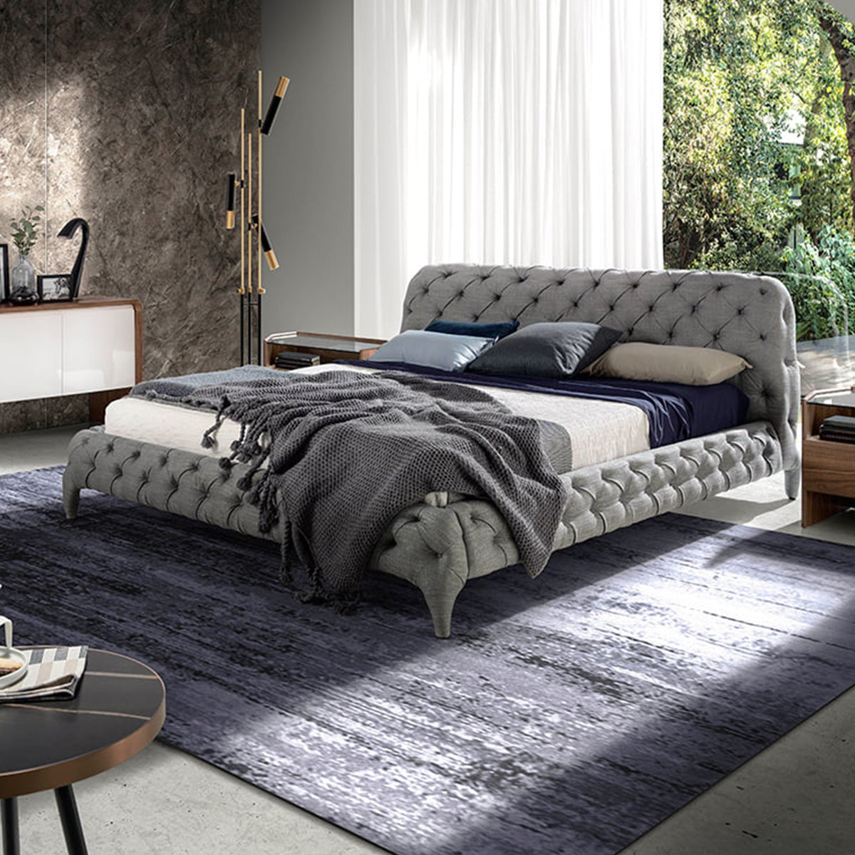 Letto Marene matrimoniale in una camera luminosa con rivestimento grigio capitonné e arredi moderni in legno.