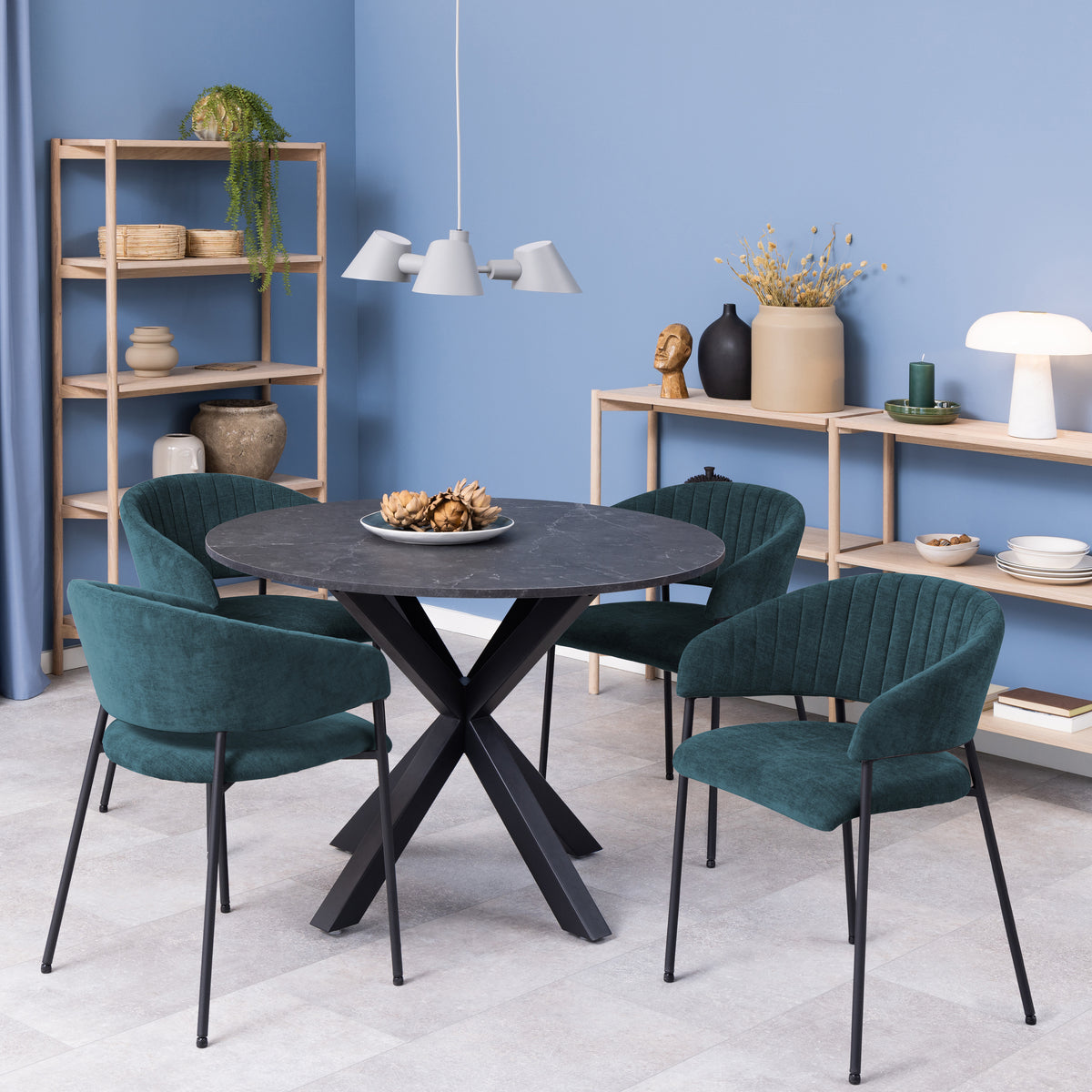 Set di sedie Brooke verde scuro attorno a un tavolo rotondo nero in un ambiente moderno con scaffali in legno.