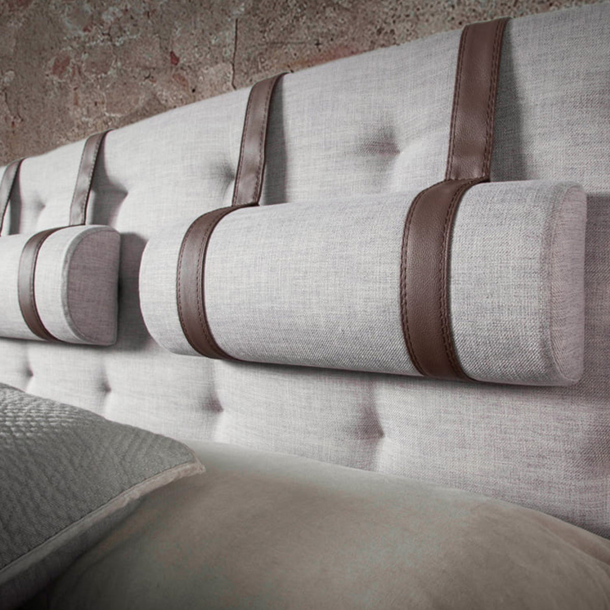 Dettaglio della testiera capitonné del Letto Lusiana, con poggiatesta cilindrici rivestiti in tessuto grigio e listelli in similpelle color cioccolato.