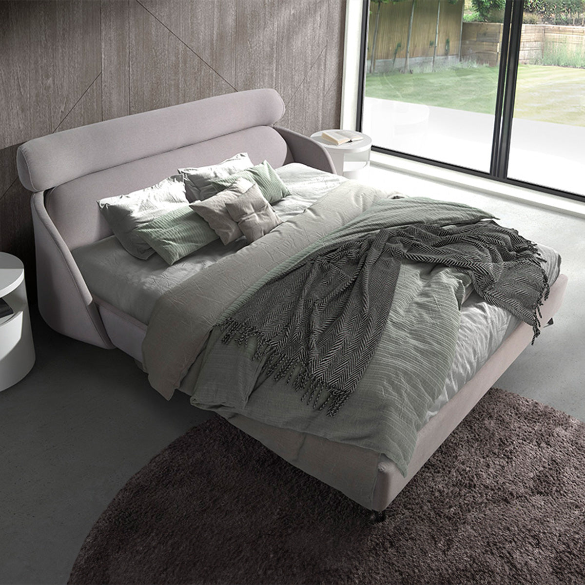 Letto Malung in una camera moderna con ampie finestre, tessuto grigio chiaro e coperte eleganti, perfetto per un ambiente accogliente.