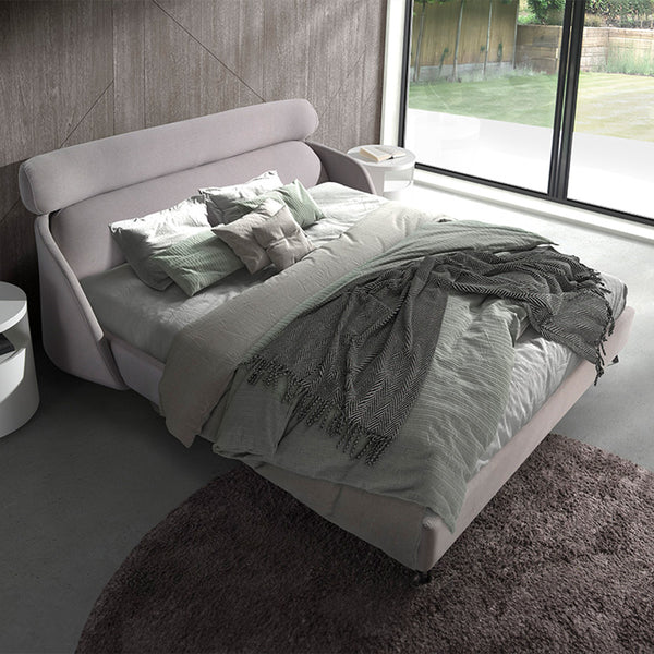 Letto Malung in una camera moderna con ampie finestre, tessuto grigio chiaro e coperte eleganti, perfetto per un ambiente accogliente.