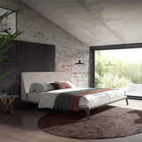 Camera da letto con Letto Mara matrimoniale, tessuto grigio, gambe in acciaio nero, ambientazione moderna con pareti in mattoni.