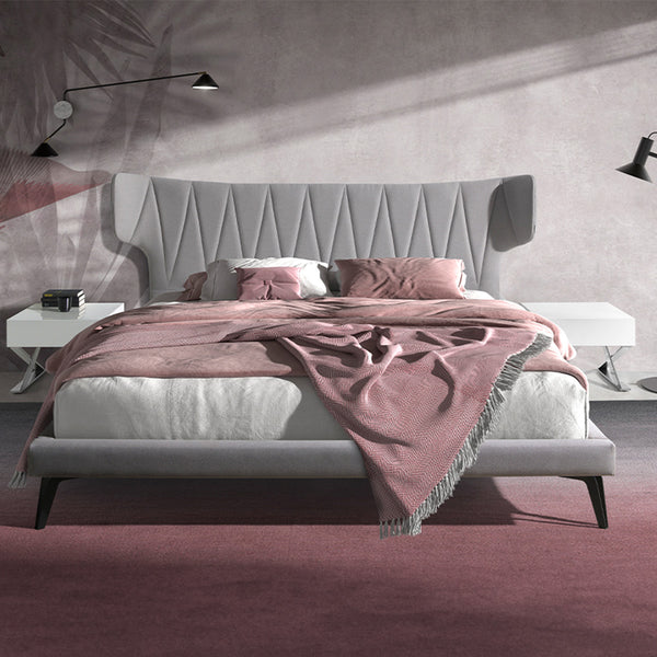 Letto Mandela in una camera da letto moderna con testata imbottita grigia, copriletto rosa e comodini bianchi, stile accogliente e raffinato.