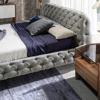 Vista ravvicinata del Letto Marene matrimoniale con rivestimento capitonné grigio, abbinato a comodini in legno.