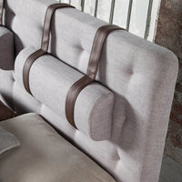 Primo piano della testiera del Letto Lusiana, con design capitonné grigio e poggiatesta cilindrici fissati con listelli in similpelle marrone.