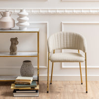 Sedia Brooke beige posizionata in un ambiente elegante con scaffale decorativo, ideale per interni moderni e raffinati.