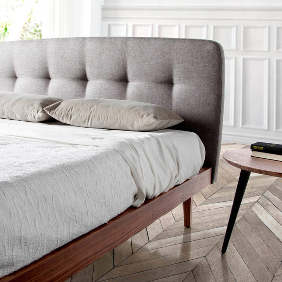 Primo piano della testiera capitonné del Letto Luxor in tessuto grigio, con struttura in legno noce.