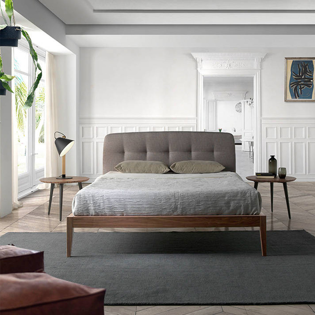 Letto Luxor in una camera moderna, con testiera capitonné grigia e struttura in legno noce, affiancato da comodini.